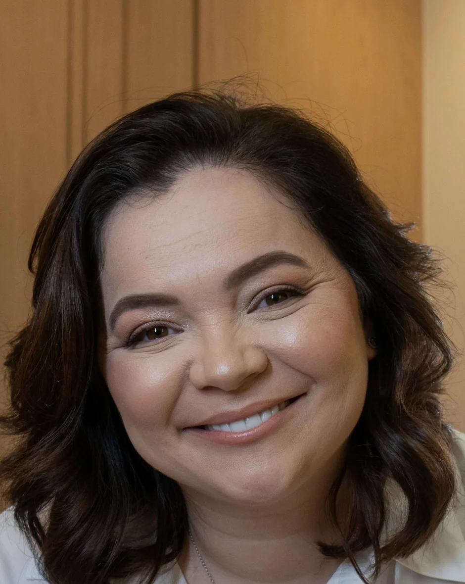 Dra. Beatriz Alves de camisa branca, sorrindo de perto, diante de um painel de carvalho